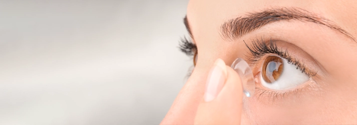 A person putting a contact in their eye. Their eye is brown.