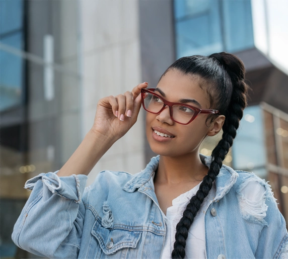 A woman in a braided ponytail smiling with maroon glasses on.